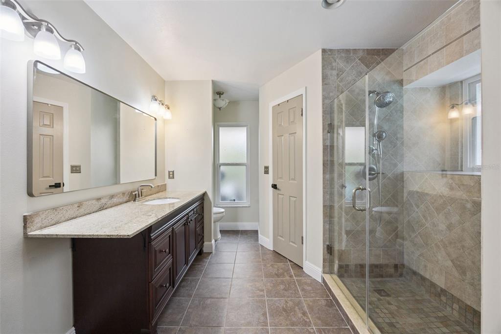 A bathroom features a dark wood vanity, granite countertop, tiled walk-in shower, and tile flooring — 680 TOMLINSON TERRACE, LAKE MARY, FL