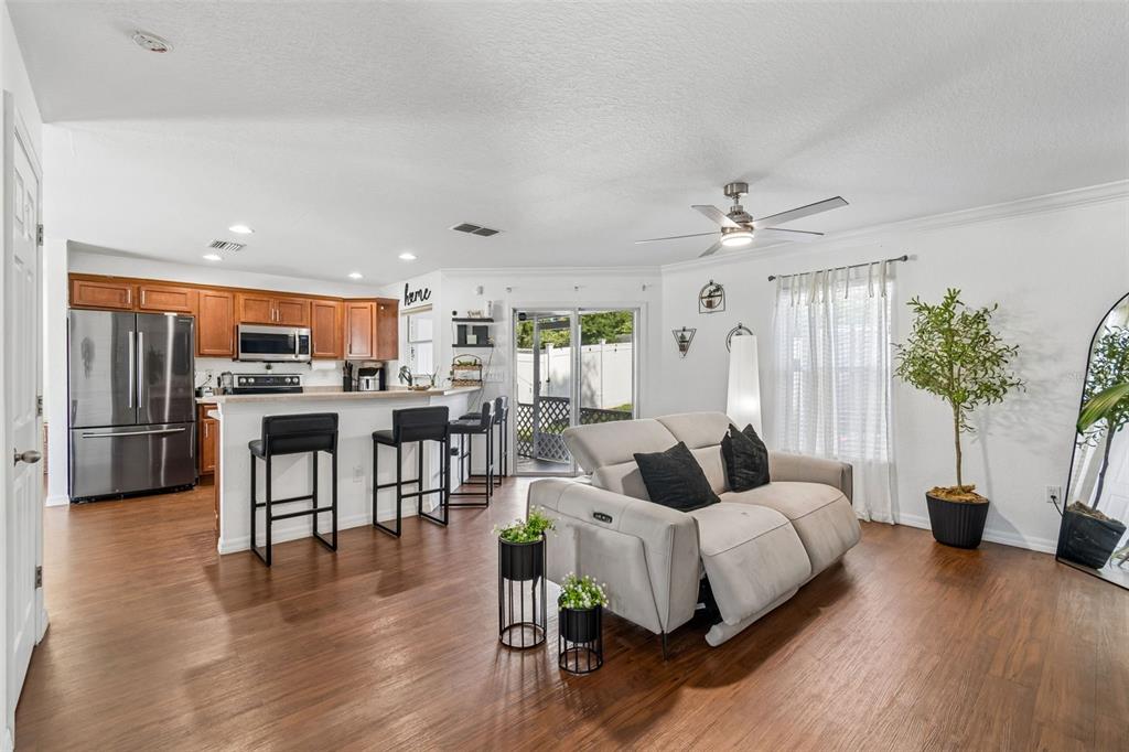 An open-concept kitchen and living area features wood-look flooring, stainless steel appliances, and a sofa — 222 CARPENTERS WAY UNIT 65, LAKELAND, FL