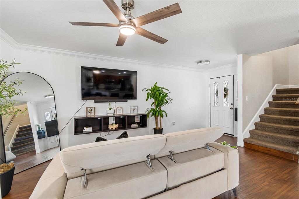 A living room features a beige sofa, wall-mounted television, floating shelf, and a staircase — 222 CARPENTERS WAY UNIT 65, LAKELAND, FL