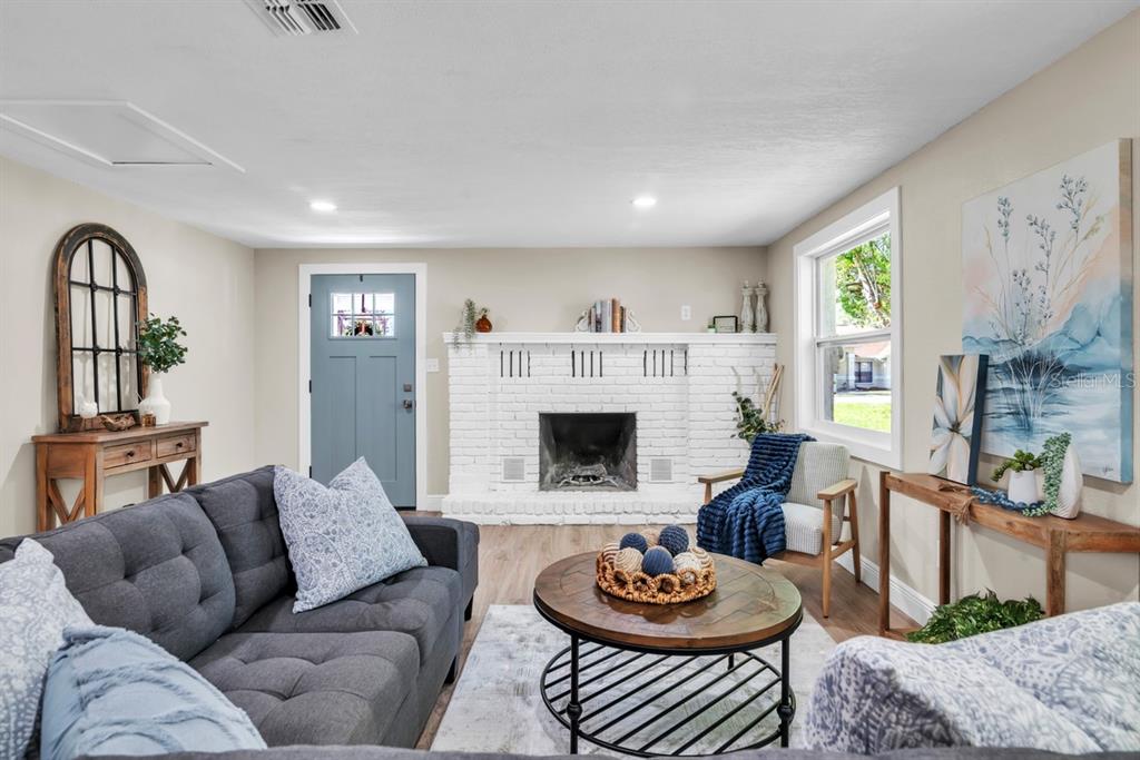 A living room features a white brick fireplace, gray sofa, and a blue front door — 11416 PINE FOREST DRIVE, NEW PORT RICHEY, FL