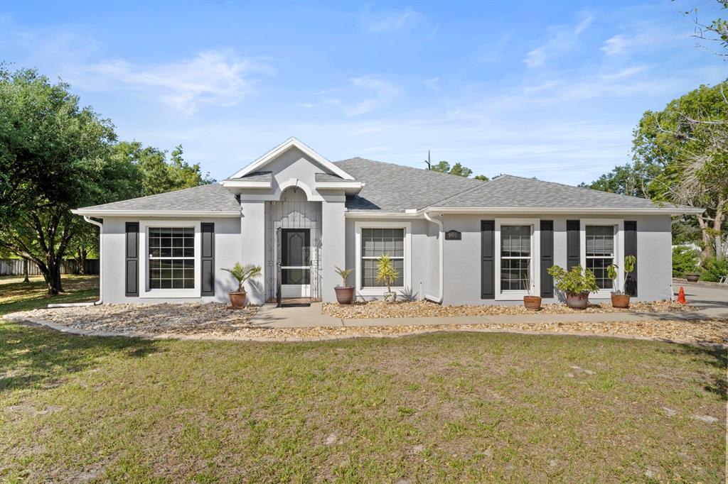 A single-story gray house with black shutters, a gabled entryway, and a gravel front yard — 900 BLANEY COURT, DELTONA, FL