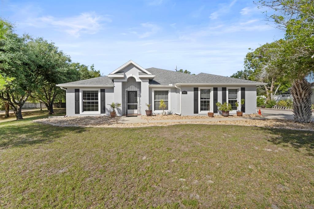 A single-story gray house with a gabled entryway and black shutters sits on a lawn — 900 BLANEY COURT, DELTONA, FL