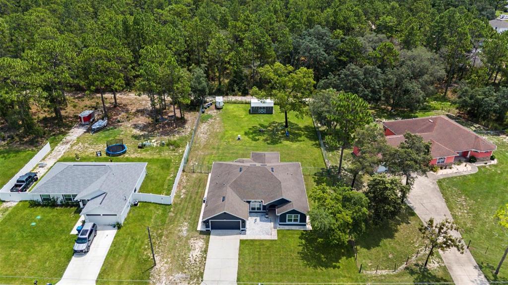 An aerial view shows three suburban houses with large backyards surrounded by dense pine trees — 12258 HARRIS HAWK ROAD, WEEKI WACHEE, FL