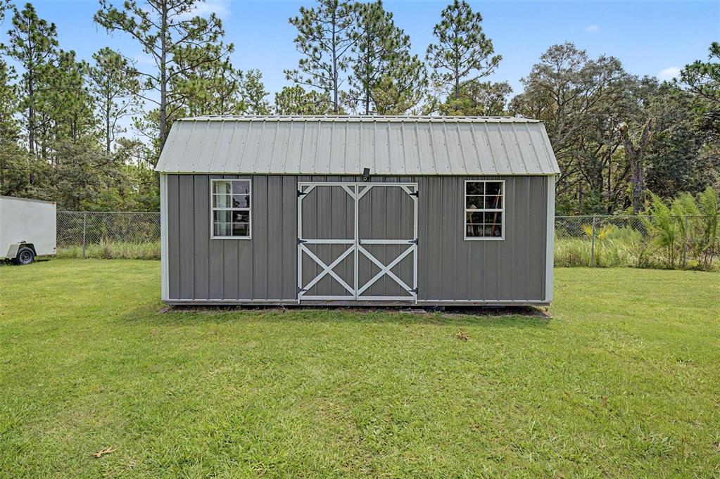 A gray metal shed with a gambrel roof stands in a grassy backyard — 12258 HARRIS HAWK ROAD, WEEKI WACHEE, FL