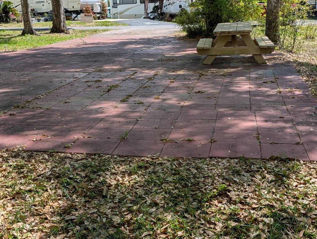 A paved patio area features a wooden picnic table situated near trees and RVs — 25215 NE 142ND STREET, SALT SPRINGS, FL
