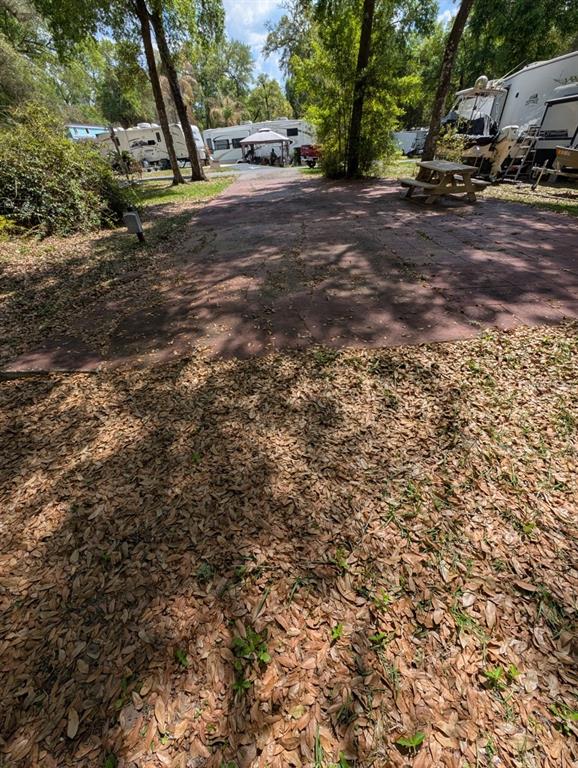 A paved campsite area features a wooden picnic table surrounded by trees and parked RVs — 25215 NE 142ND STREET, SALT SPRINGS, FL