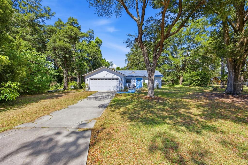 A single-story house with a white garage and blue front door sits on a wooded lot — 3880 NE 22ND COURT, OCALA, FL