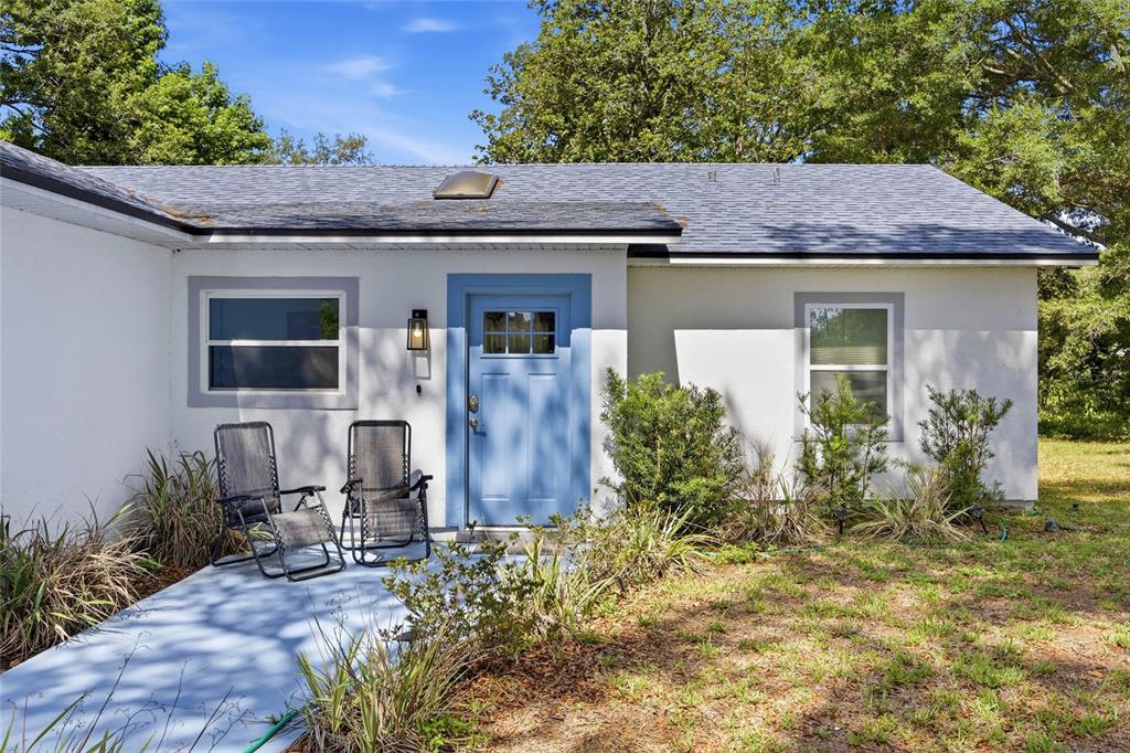 A single-story house exterior features a blue front door, two patio chairs, and landscaping — 3880 NE 22ND COURT, OCALA, FL