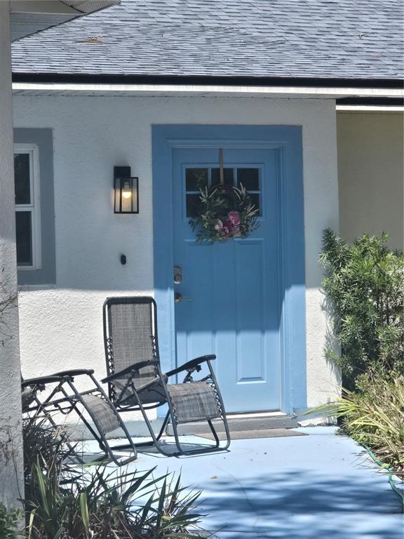 A light blue front door with a wreath sits on a porch with two chairs — 3880 NE 22ND COURT, OCALA, FL