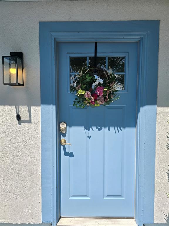 A light blue front door with a floral wreath sits in a white stucco wall — 3880 NE 22ND COURT, OCALA, FL