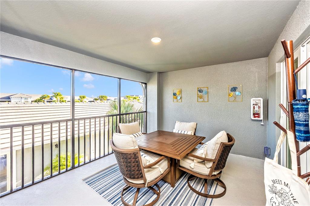 A screened-in balcony features a wooden dining set on a striped rug — 17500 OPAL SAND COURT UNIT 207, VENICE, FL