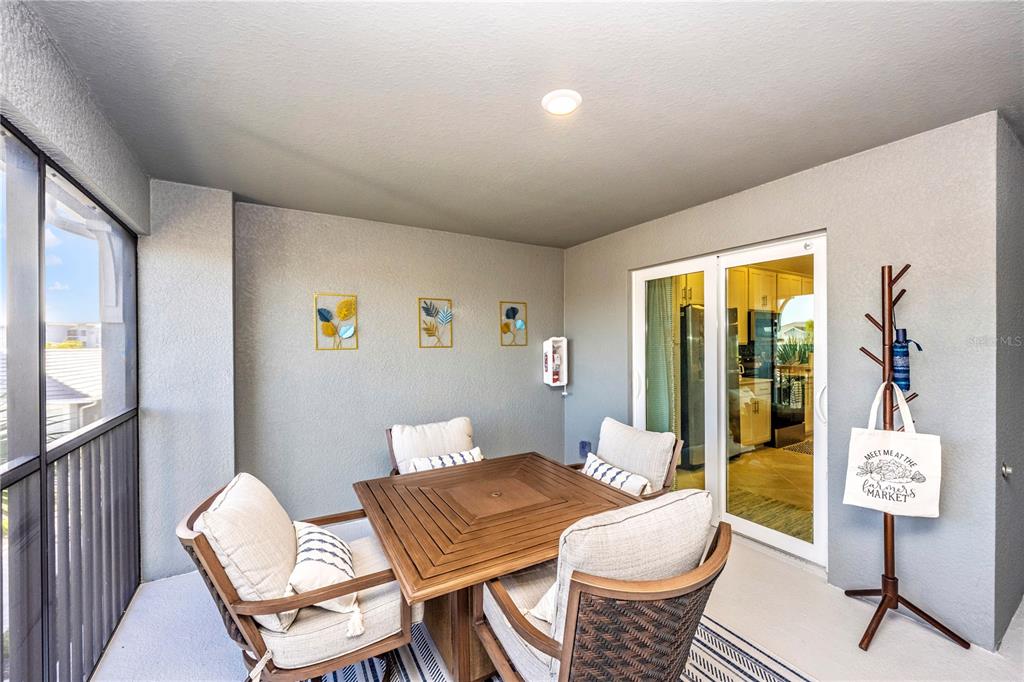 A covered patio features a wooden dining set, wall art, and a coat rack — 17500 OPAL SAND COURT UNIT 207, VENICE, FL