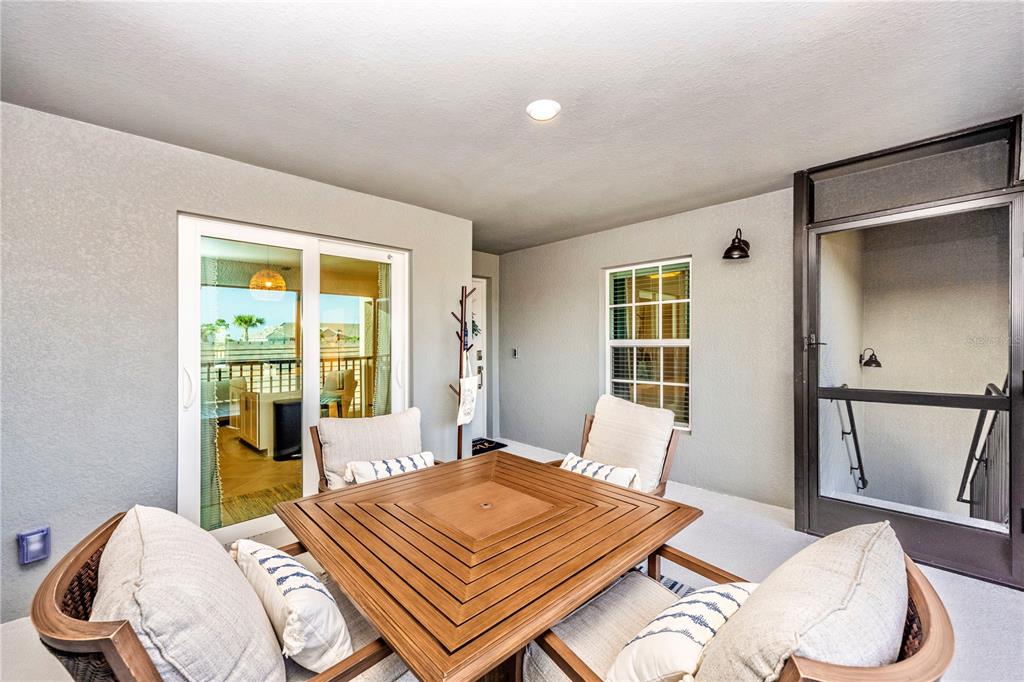A covered patio features a wooden table with chairs, a sliding glass door, and a screen door — 17500 OPAL SAND COURT UNIT 207, VENICE, FL
