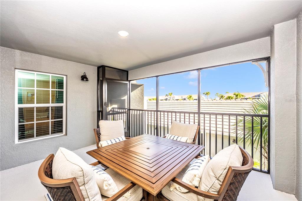 A screened-in balcony features a square wooden table with four cushioned chairs — 17500 OPAL SAND COURT UNIT 207, VENICE, FL