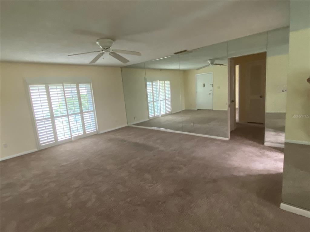 A living room features beige carpeting, a ceiling fan, and a large mirrored wall — 1500 GAY ROAD UNIT 17D, WINTER PARK, FL