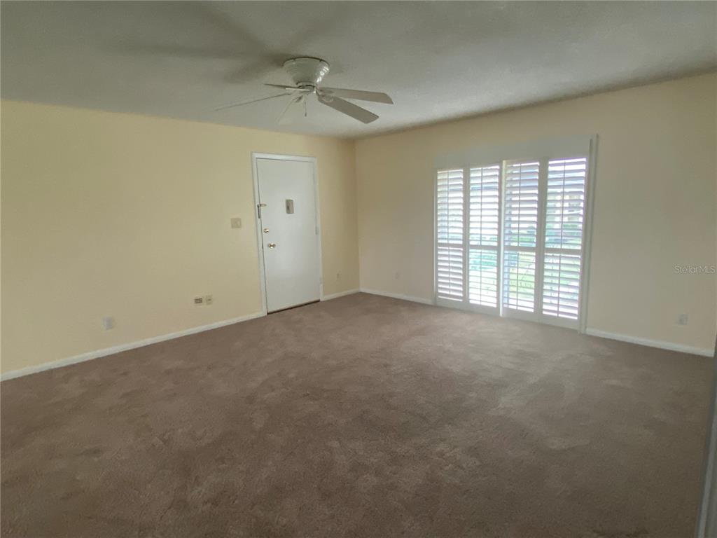 An empty room features beige carpet, a ceiling fan, a white door, and plantation shutters — 1500 GAY ROAD UNIT 17D, WINTER PARK, FL