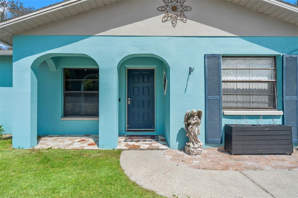 A turquoise house exterior features an arched entryway, a dark blue door, and a stone patio — 12989 LINDEN DRIVE, SPRING HILL, FL