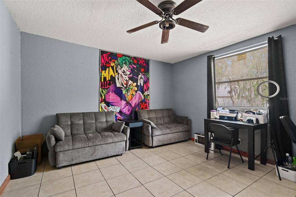 A bedroom with gray walls, tile flooring, two gray sofas, and a Joker wall poster — 12989 LINDEN DRIVE, SPRING HILL, FL
