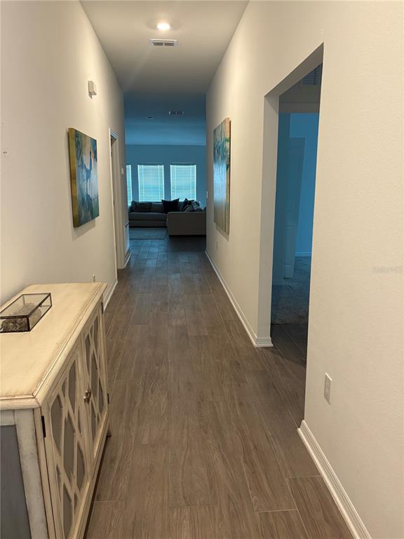 A hallway with wood-look tile flooring leads toward a living area with a sofa — 309 SINGING SANDS CIRCLE, LAKE WALES, FL