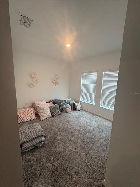 A carpeted bedroom features white walls, two windows with blinds, and several floor pillows — 309 SINGING SANDS CIRCLE, LAKE WALES, FL