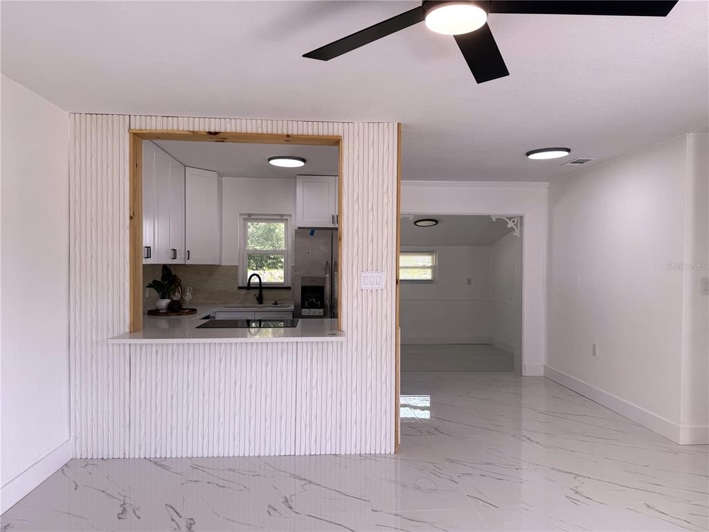 A kitchen with white cabinets and a pass-through window overlooks a room with tiled floors — 4100 GARDEN STREET, TITUSVILLE, FL