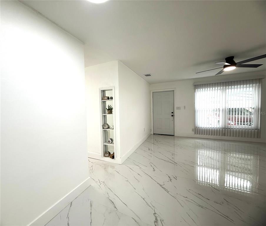 A bright living area features white marble-look tile flooring, a ceiling fan, and built-in shelving — 4100 GARDEN STREET, TITUSVILLE, FL