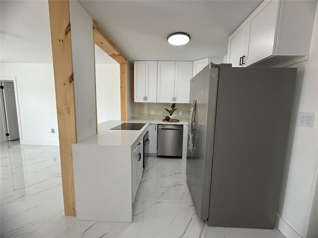 A modern kitchen features white cabinets, stainless steel appliances, and a white quartz countertop peninsula — 4100 GARDEN STREET, TITUSVILLE, FL