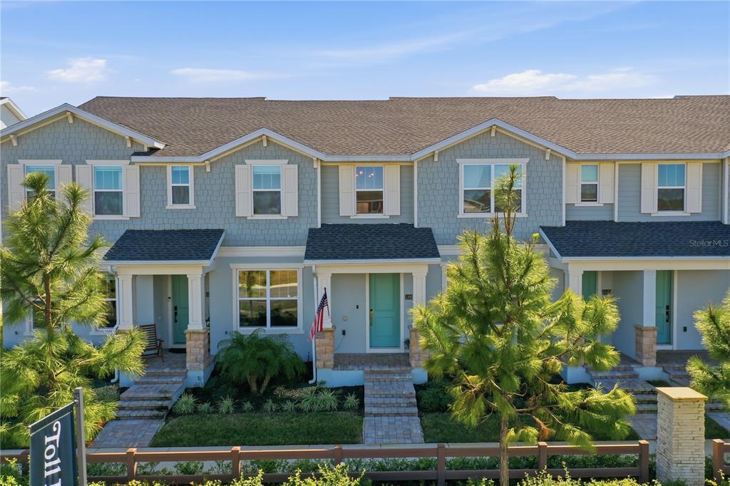 A row of multi-story townhomes with light blue siding, stone accents, and teal front doors — 13953 EASDALE ALLEY, WINTER GARDEN, FL