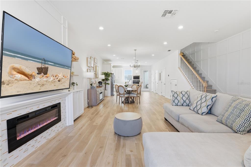 An open-concept living room and dining area features light wood floors, a fireplace, and stairs — 13953 EASDALE ALLEY, WINTER GARDEN, FL