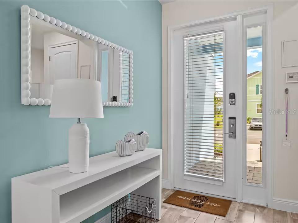 An entryway features a white console table, a lamp, a mirror, and a glass-paneled door — 3193 CARIBBEAN SOUL DRIVE, KISSIMMEE, FL