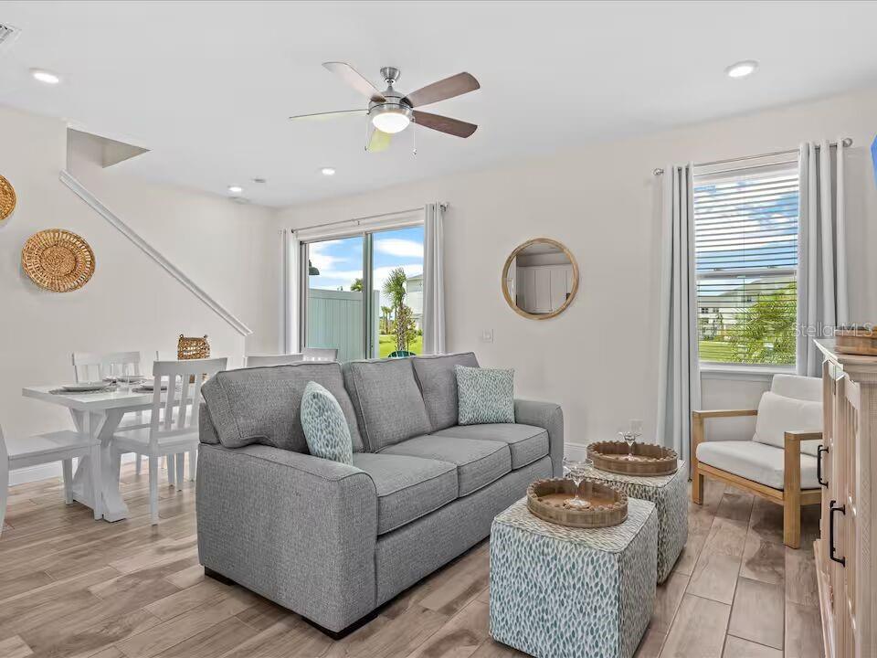 A living room with a gray sofa, two patterned ottomans, and a dining area nearby — 3193 CARIBBEAN SOUL DRIVE, KISSIMMEE, FL