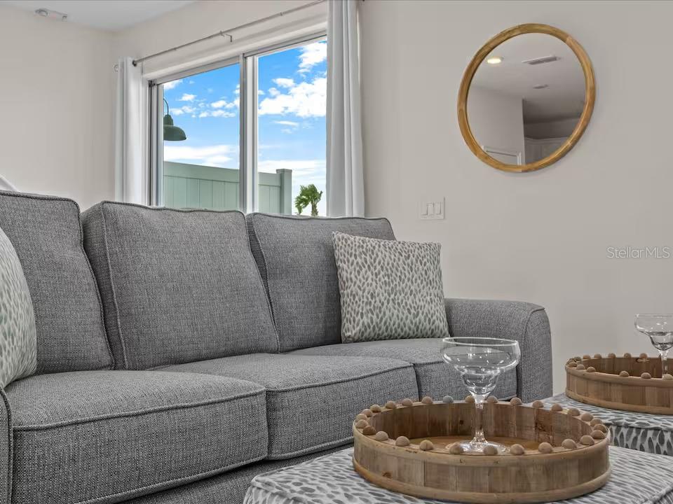 A gray sofa sits in a living room with a round mirror and wooden trays — 3193 CARIBBEAN SOUL DRIVE, KISSIMMEE, FL