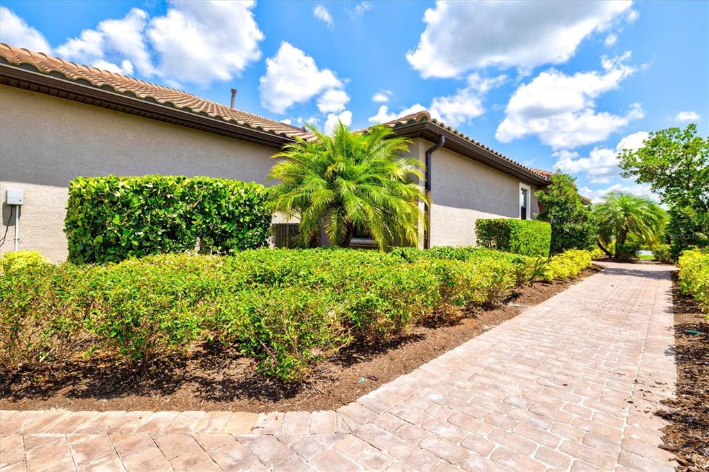 A paved walkway leads past a landscaped garden and a house with a tiled roof — 10254 MORNING MIST LANE, SARASOTA, FL