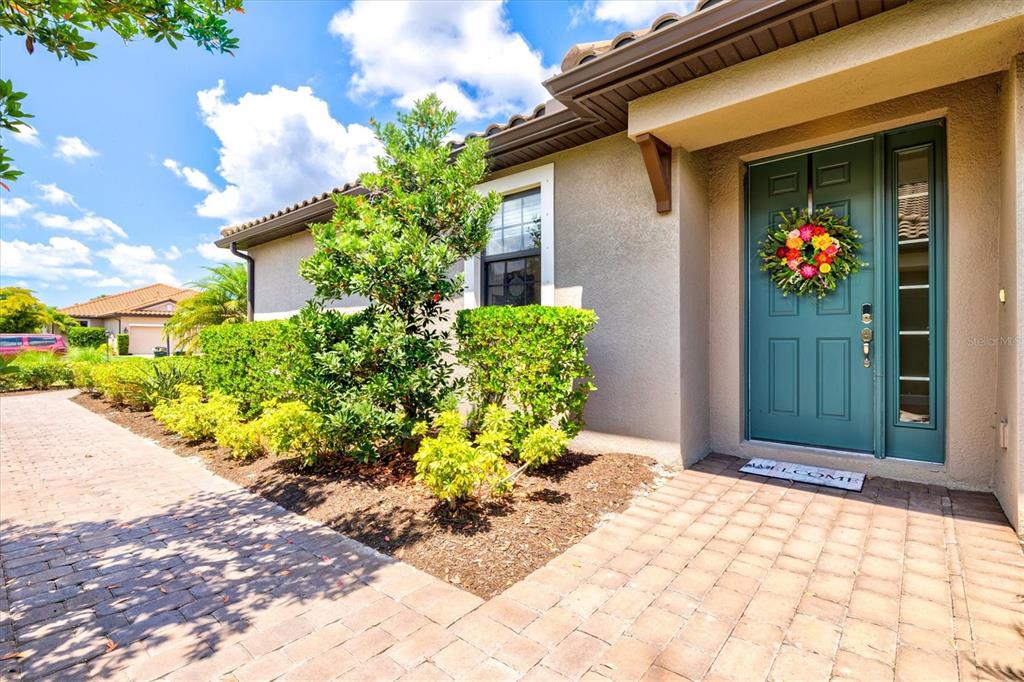 A teal front door with a floral wreath sits beside a brick walkway and landscaping — 10254 MORNING MIST LANE, SARASOTA, FL