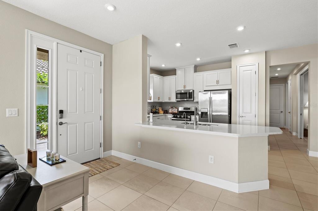 A bright entryway leads to an open kitchen with white cabinets and a breakfast bar — 10254 MORNING MIST LANE, SARASOTA, FL