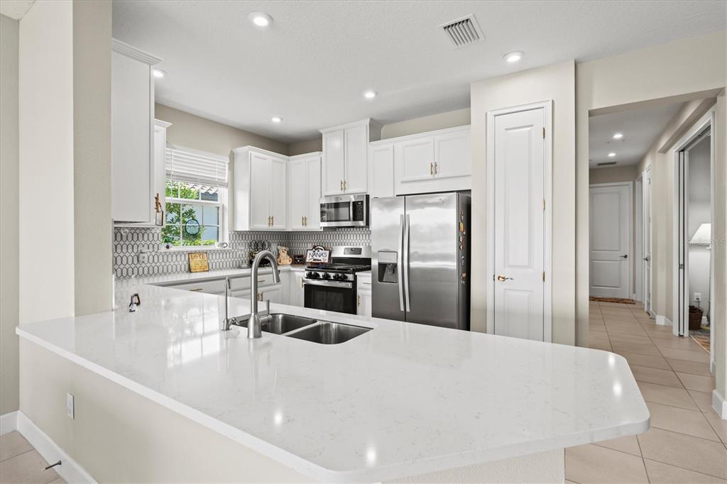 A kitchen features white cabinets, stainless steel appliances, and a white quartz-topped island — 10254 MORNING MIST LANE, SARASOTA, FL