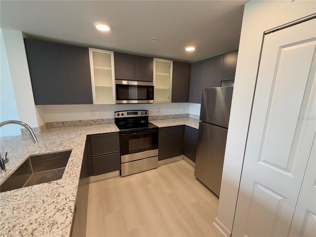 A modern kitchen features dark gray cabinets, granite countertops, and stainless steel appliances — 5587 MILLENIA PARK BLVD UNIT 217, ORLANDO, FL