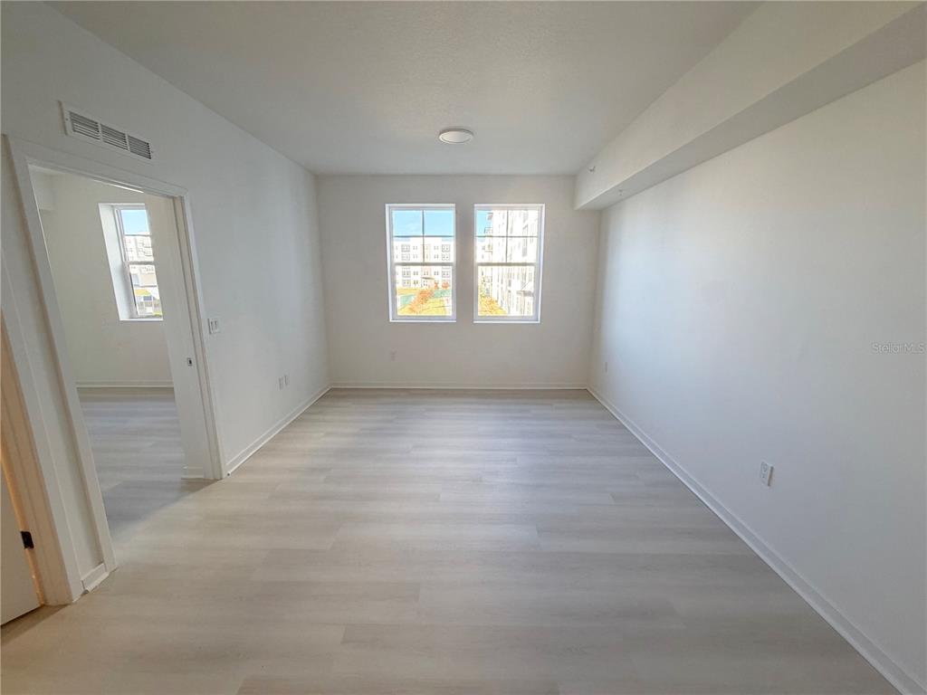 An empty room features light wood-look flooring, white walls, and two windows facing outside — 5587 MILLENIA PARK BLVD UNIT 217, ORLANDO, FL