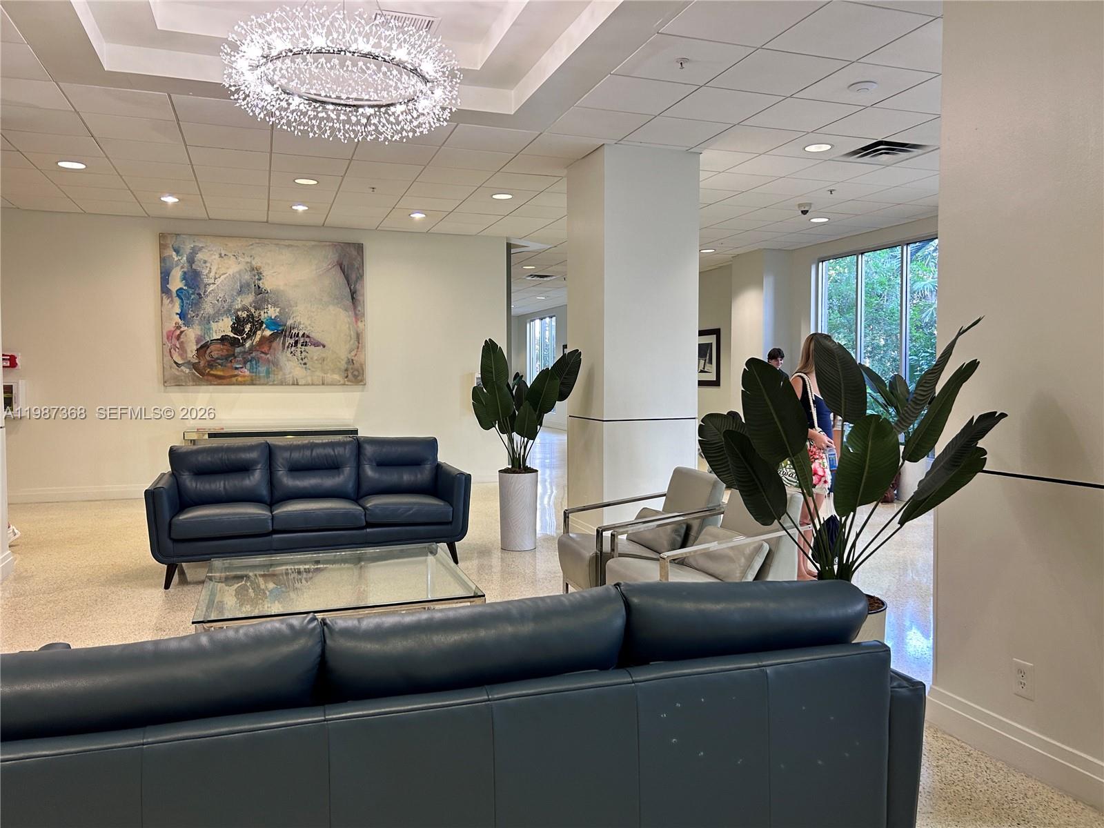 A modern lobby features blue leather sofas, a glass coffee table, and a large chandelier — 4001 S Ocean Dr # 4G, Hollywood FL 33019, HOLLYWOOD, FL