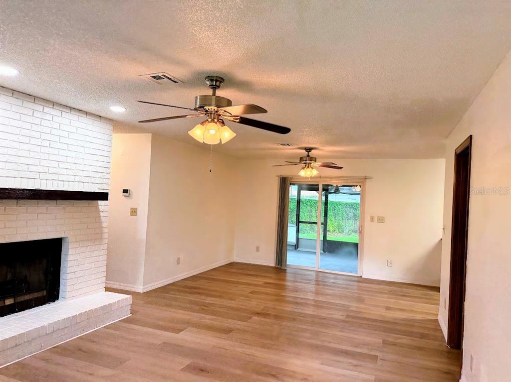 A living room features a white brick fireplace, wood-look flooring, and two ceiling fans — 601 NE 27TH STREET, OCALA, FL