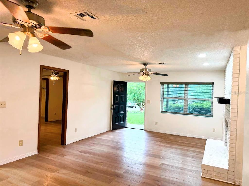 A living room with wood-look flooring, two ceiling fans, a fireplace, and an open door — 601 NE 27TH STREET, OCALA, FL