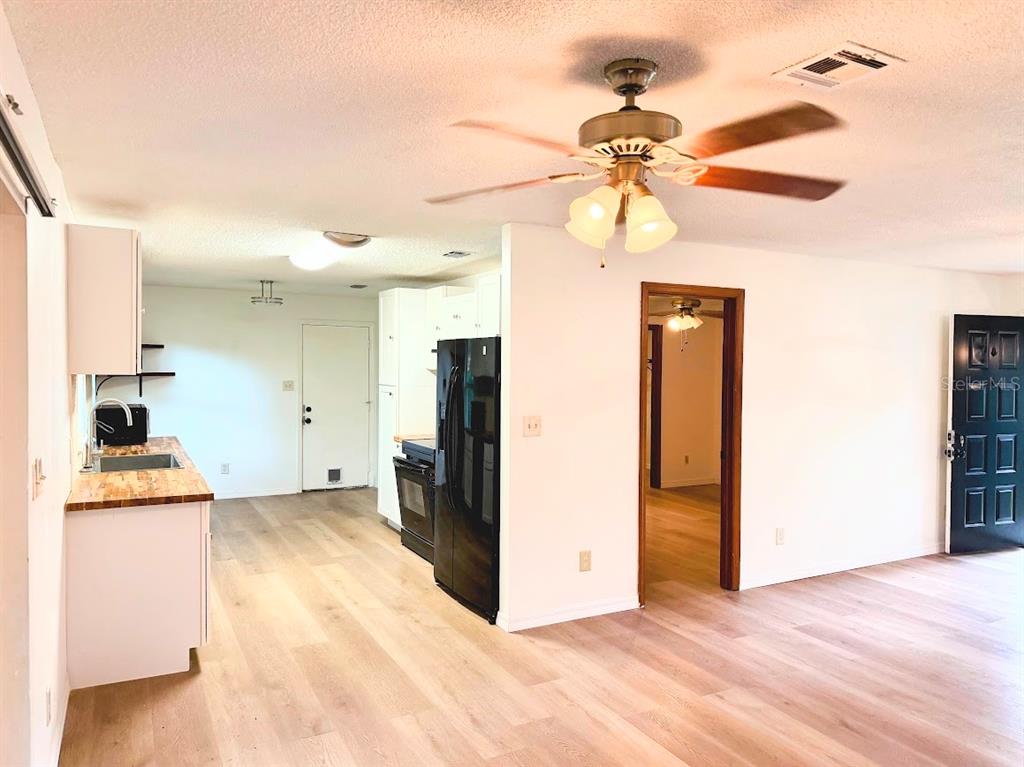 A kitchen with light wood flooring and a black refrigerator opens into a living area — 601 NE 27TH STREET, OCALA, FL