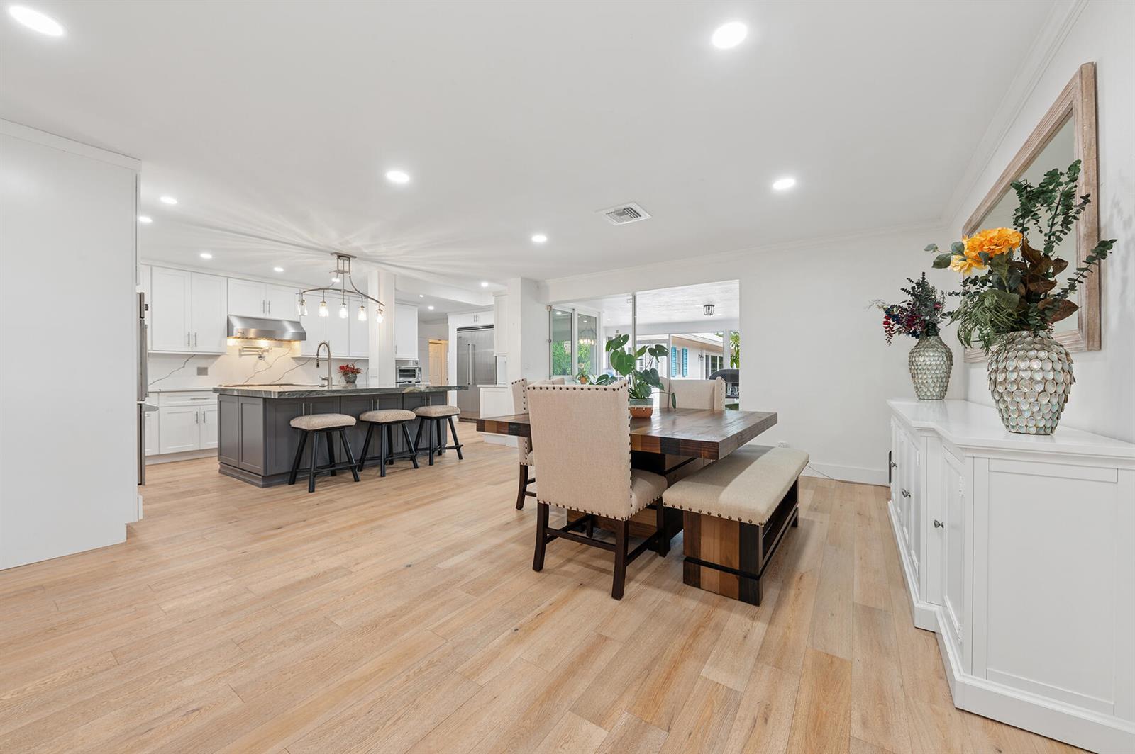 An open-concept kitchen and dining area featuring light wood floors and a dark kitchen island — 2001 NW 1st Avenue, Delray Beach FL 33444, DELRAY BEACH, FL