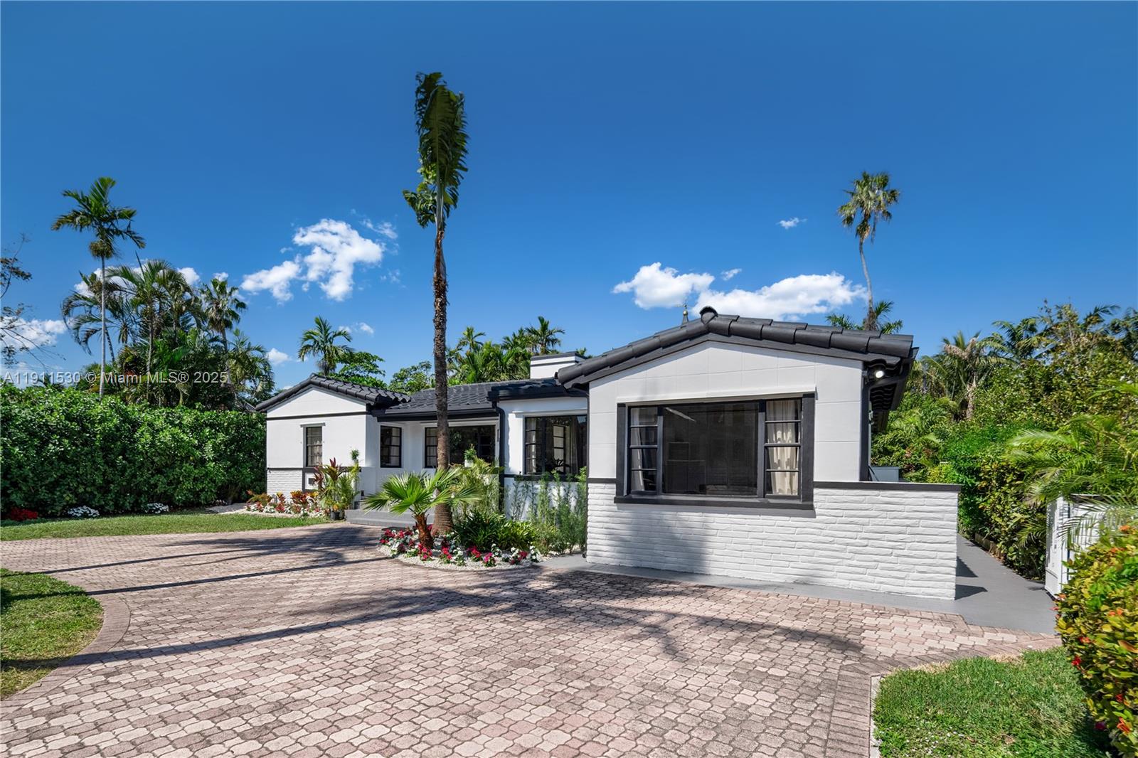 A white, single-story house with a dark roof and brick accents sits behind a paved driveway — 118 E 3rd Ct, Miami Beach FL 33139, MIAMI BEACH, FL