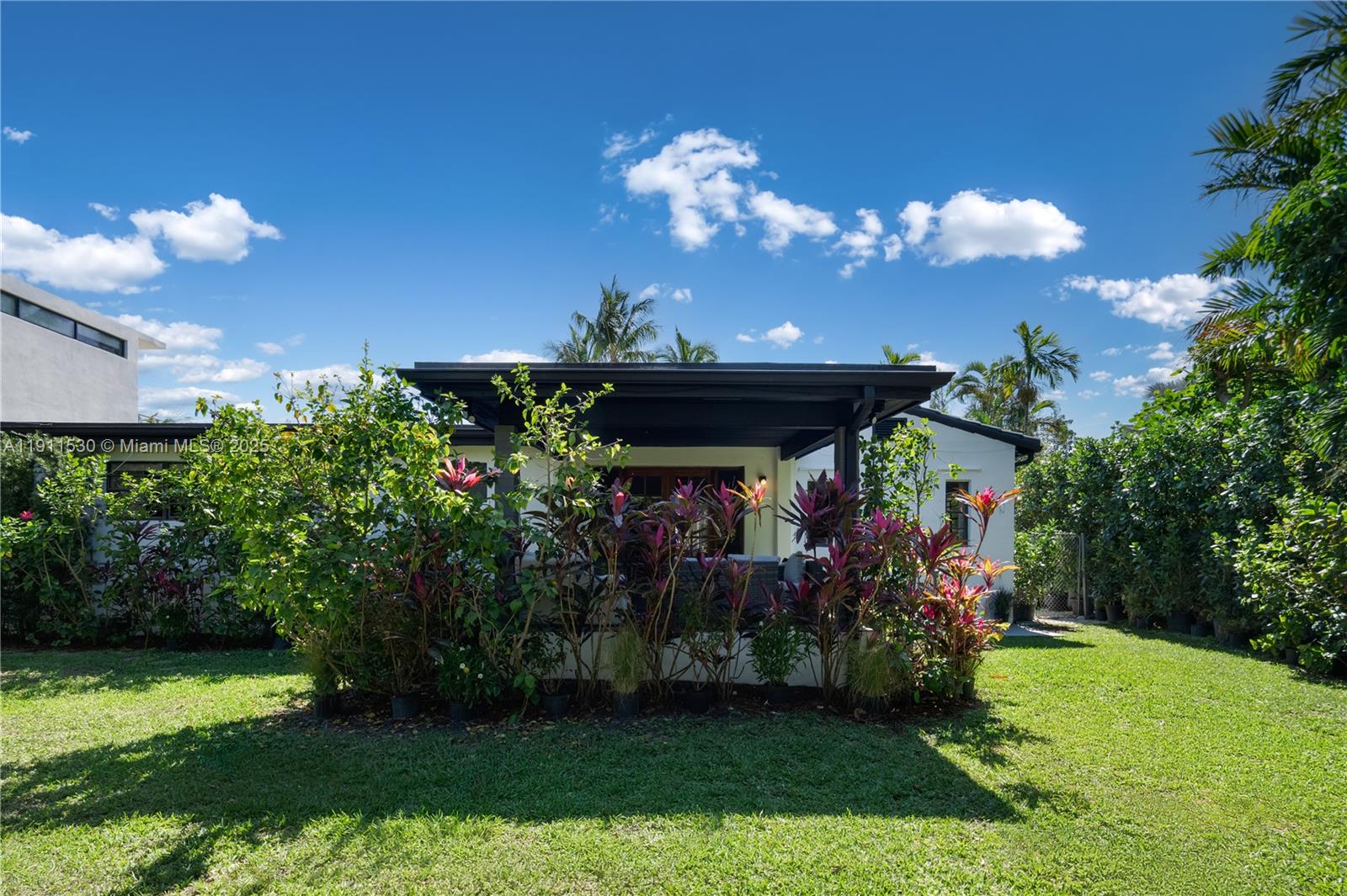 A backyard view of a white house with a covered patio and tropical landscaping — 118 E 3rd Ct, Miami Beach FL 33139, MIAMI BEACH, FL