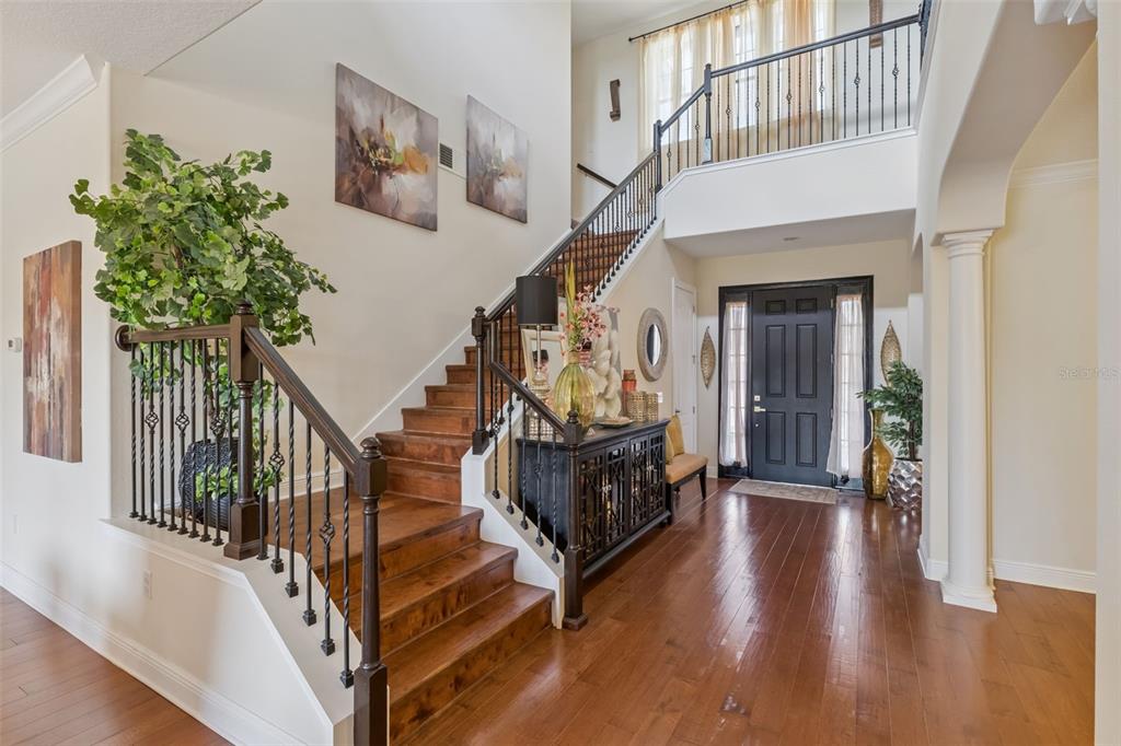A foyer features hardwood floors, a staircase with iron railings, and a dark front door — 4117 FOXHOUND DRIVE, CLERMONT, FL