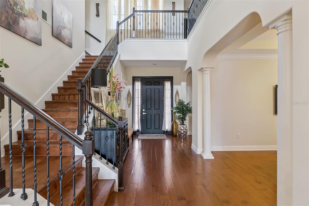 A foyer features hardwood floors, a dark front door, and a staircase with iron railings — 4117 FOXHOUND DRIVE, CLERMONT, FL
