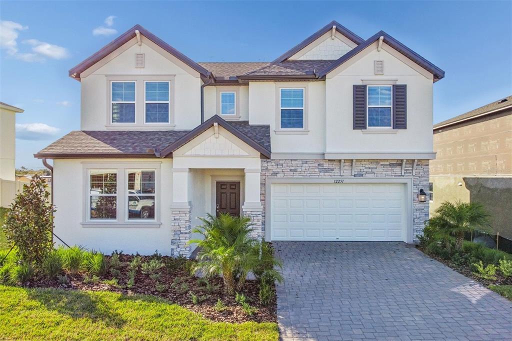 A two-story suburban house features a stone-accented facade, a paved driveway, and a garage — 12251 STIRRUP DRIVE, DADE CITY, FL