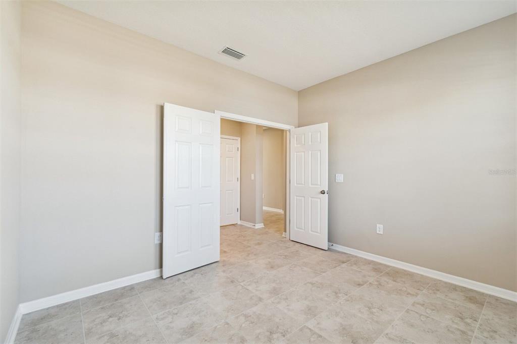 A room with beige walls, tile flooring, and double doors opening to a hallway — 12251 STIRRUP DRIVE, DADE CITY, FL