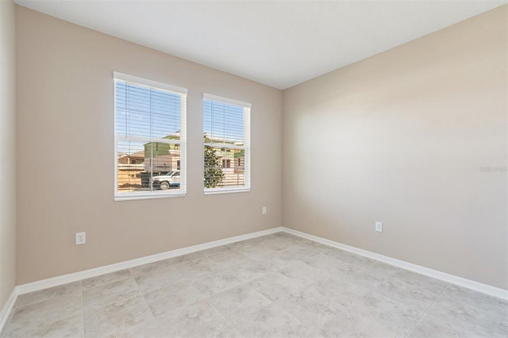 An empty room with beige walls, tile flooring, and two windows overlooking a construction site — 12251 STIRRUP DRIVE, DADE CITY, FL